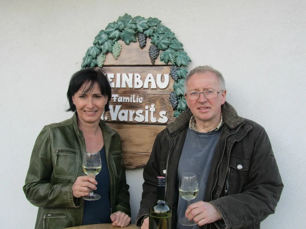 Martina und Michael Varsits mit Gläsern Weißwein vor dem Weinbau-Schild